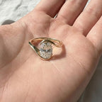 Oval cut diamond bypass engagement ring with asymmetrical open wrap gold band and modern solitaire setting.