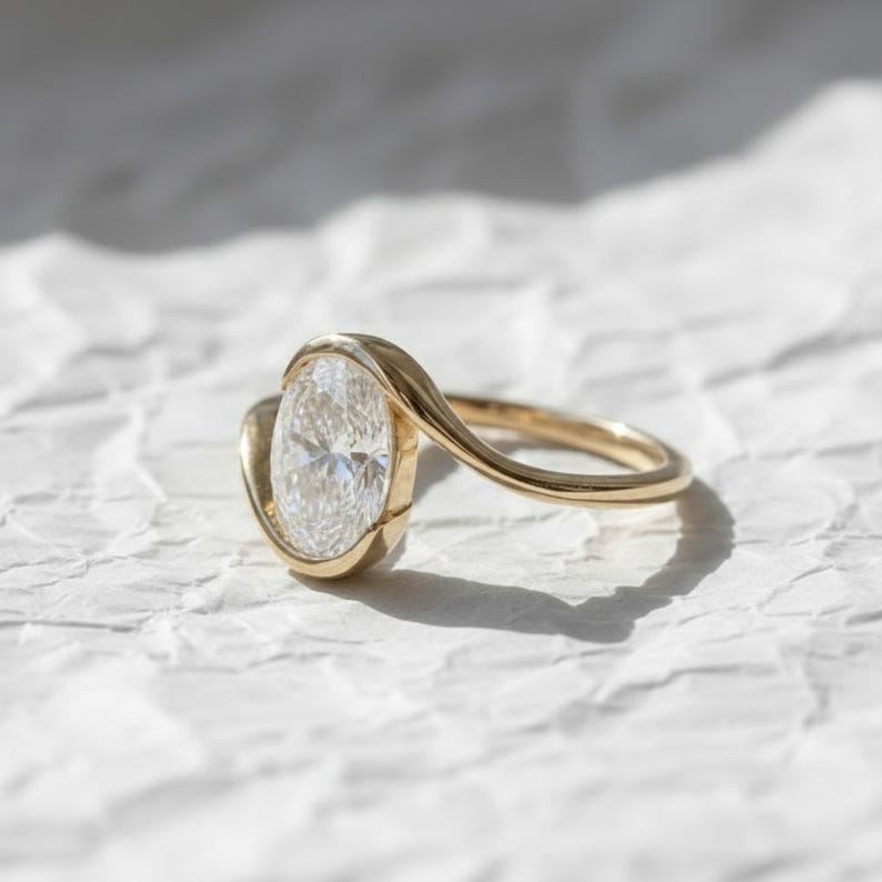 Oval cut diamond bypass engagement ring with asymmetrical open wrap gold band and modern solitaire setting.