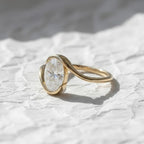Oval cut diamond bypass engagement ring with asymmetrical open wrap gold band and modern solitaire setting.