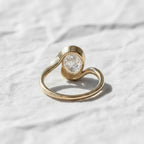 Oval cut diamond bypass engagement ring with asymmetrical open wrap gold band and modern solitaire setting.
