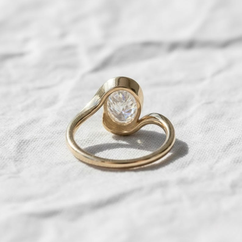 Oval cut diamond bypass engagement ring with asymmetrical open wrap gold band and modern solitaire setting.