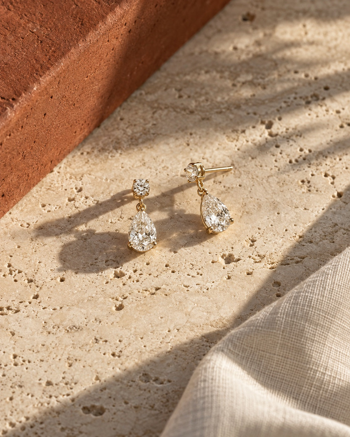 ÉLYSÉA campaign pear-drop earrings on warm travertine